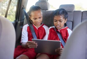 Children, friends and tablet in car entertainment, online streaming or social media. Kids enjoying games or apps while relaxing in seat on touchscreen